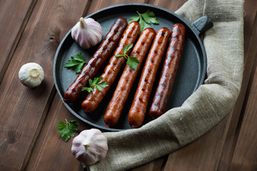 Frying pan with grilled sausages over rustic wooden background