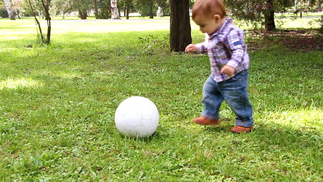Cute little boy playing with soccer ball supported by his mother