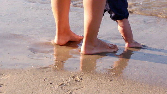Mother helping his little son making first steps on the beach
