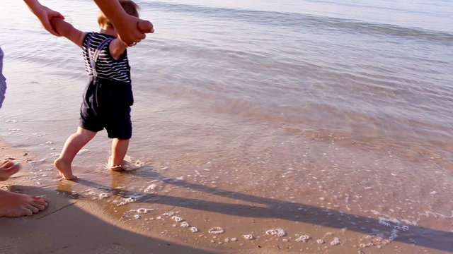 Mother helping his little son making first steps on the beach