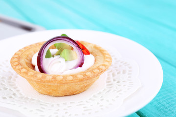 Tartlet with greens and vegetables with sauce on plate on table