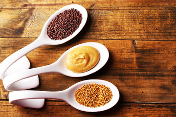 Mustard seeds, powder and sauce in spoons on wooden background