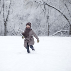 Fototapeta na wymiar Happy little girl running on the background of snow covered wint