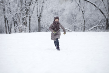 Fototapeta na wymiar Happy little girl running on the background of snow covered wint