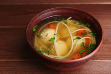 Soup with meatballs and noodles in bowl on wooden background