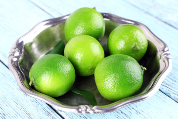 Fresh juicy limes on plate on wooden background