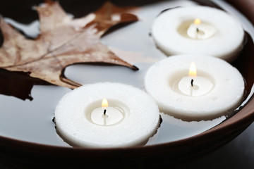 Tree white candles floating with leaf on water in bowl