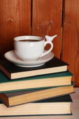 Pile of books with cup on tabletop and wooden background