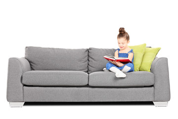 Adorable little girl reading a book on sofa