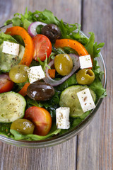 Greek salad in glass dish on wooden table background
