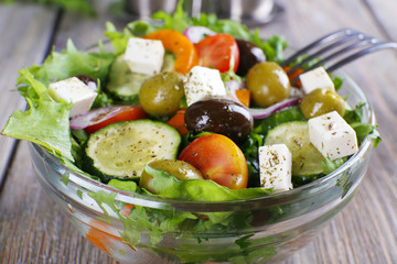 Greek salad in glass dish with fork on wooden table background