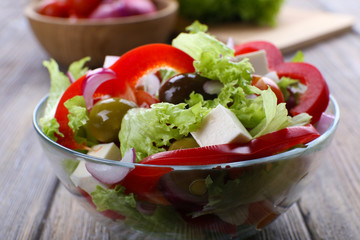 Greek salad in glass dish on wooden table background