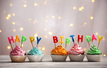 Delicious birthday cupcakes on table on light background