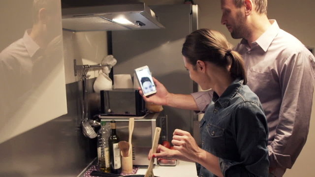 Couple video chat on smartphone and cooking in kitchen 