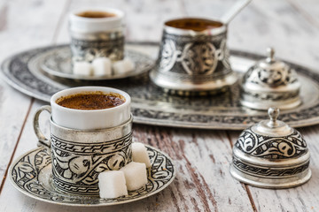 Traditional Turkish coffee in traditional silver cups on white wooden table