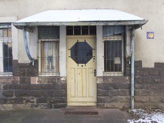 Überdachter alter Hauseingang mit Haustür aus Holz und Schnee auf dem Vordach im Winter in...