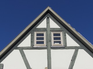 Spitzgiebel eines Fachwerkhaus mit Zwillingsfenster vor blauem Himmel im Sonnenschein in...