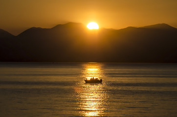 Sunset, lake sparkling.Fishermen driving a small fishing boat