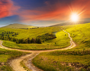 Fototapeta premium cross road on hillside meadow in mountain at sunrise at sunset