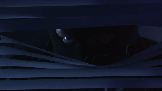 Man in mask looking through blinds on window