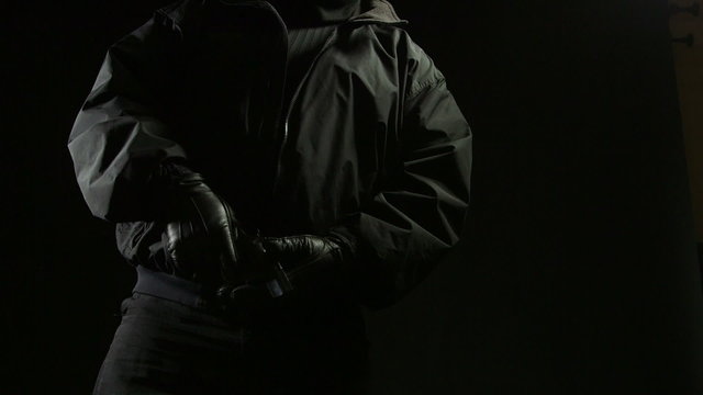 Man pulling out a gun from his jacket pocket in the darkness