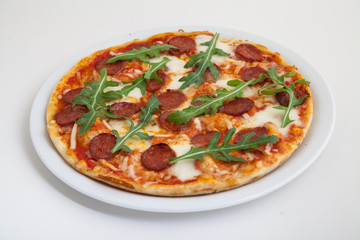 pizza with salami, cheese and arugula on white plate