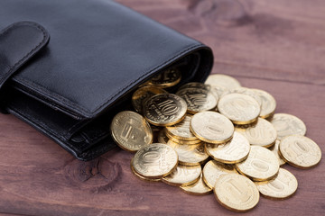 Black leather wallet with golden coins on wood background