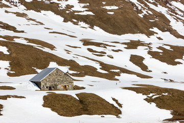 Alpine mountain landscape with cottage, snow is melting away