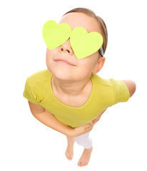 Little girl is holding hearts over her eyes