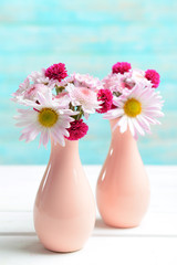 Beautiful flowers in vases on table on light blue background
