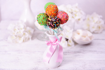 Sweet cake pops in vase on table on light background