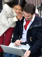 Young couple smiling and looking at laptop outdoors