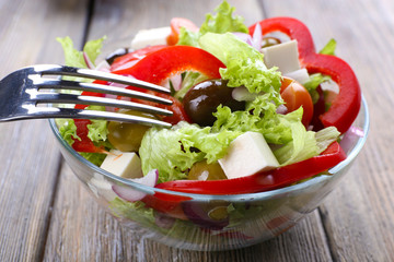 Greek salad in glass dish with fork on wooden table background