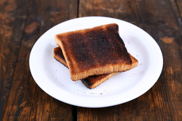 Burnt toast bread on plate, on wooden table background