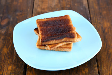 Burnt toast bread on turquoise plate, on wooden table