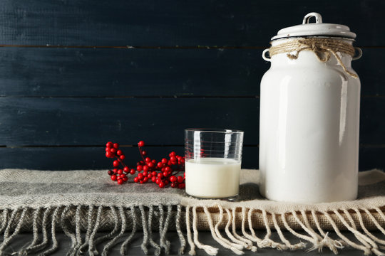 Milk can and glass with rowan on color wooden background