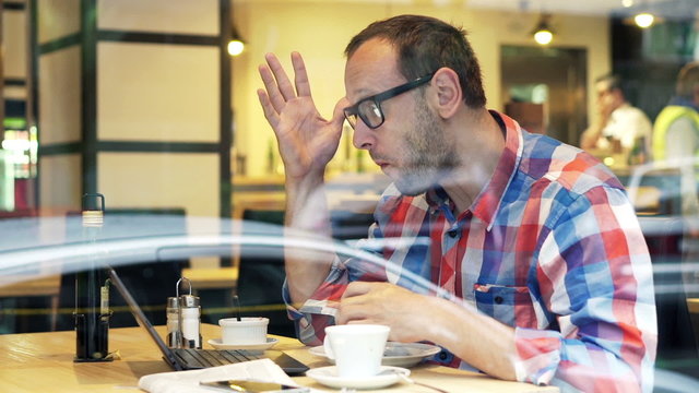 Shocked, unhappy man checking results on laptop sitting in cafe