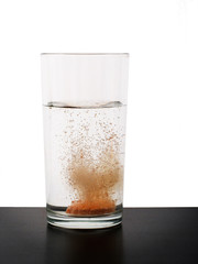 Vitamin tablet dissolving in glass of water. Fizzing.