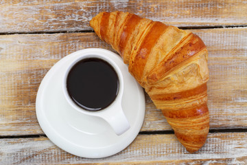 Coffee and croissant on rustic wooden surface