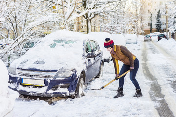 Beautiful young woman shoveling her car