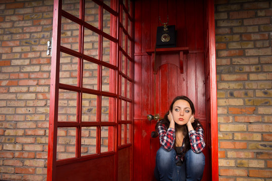 Troubled Woman Crouching in Red Telephone Booth