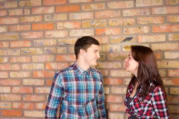 Smiling Couple Facing Each Other near Brick Wall