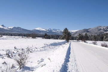 Fototapeta na wymiar Snowy road in winter sunny day prepared for car traffic