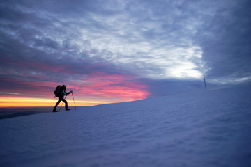 Man walking in the mountains by sunset on snowshoes.
