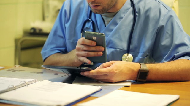 Young male doctor sitting with smartphone in the hospital