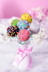Sweet cake pops in vase on table on pink background