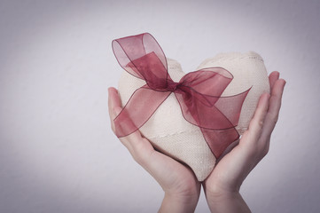 Hands holding a white fabric heart with a red ribbon