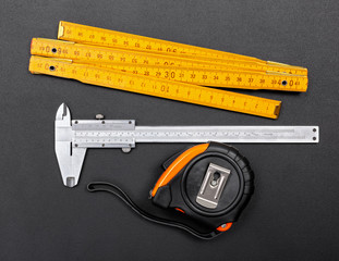 Measuring tools on black: ruler, caliper and tape