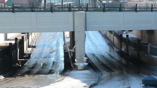Cars pass under a bridge followed by pigeons