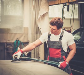 Young serviceman performing grinding  on a car bonnet 